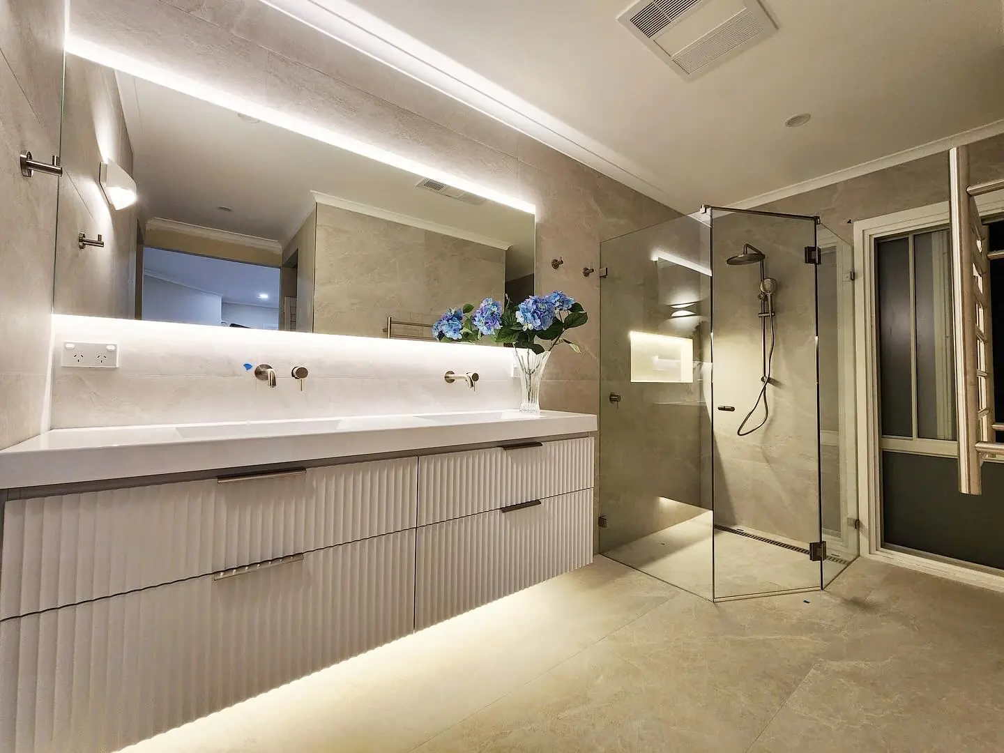 Renovated bathroom with a long vanity and illuminated mirror