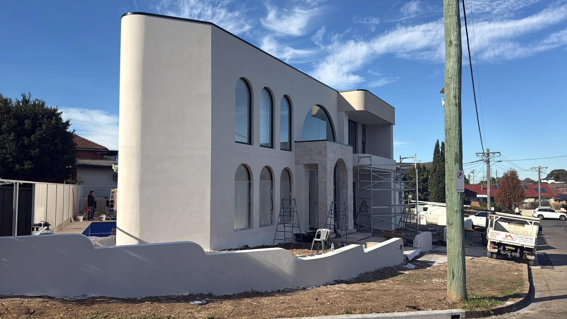 Curved rendered facade with arched windows and stone entrance during construction