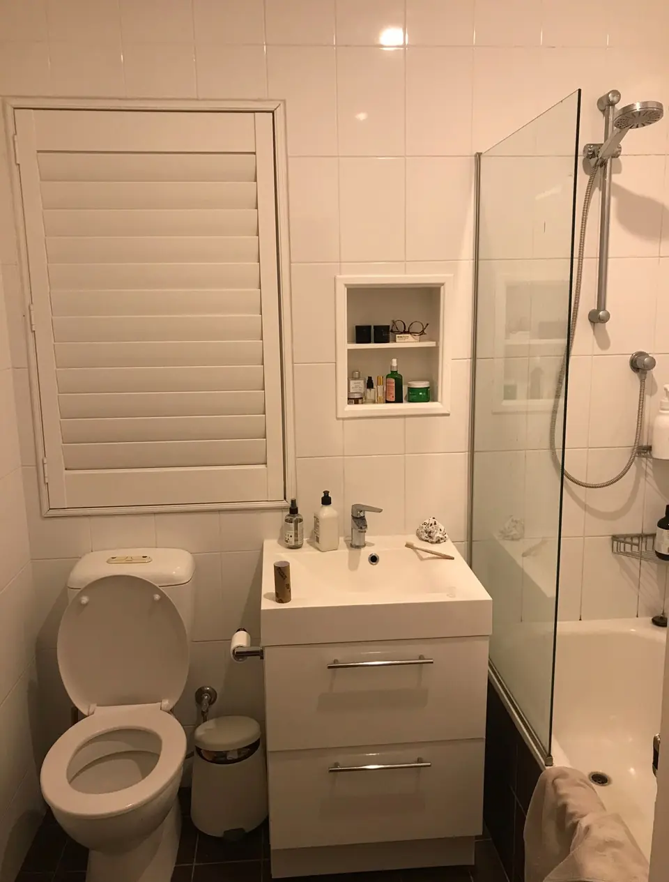 Bathroom before renovation with a white vanity and shower over the bath